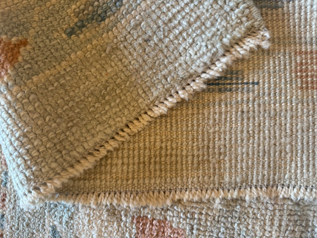 Corner of a hand-knotted rug folded back showing the border pattern continuing through the weave